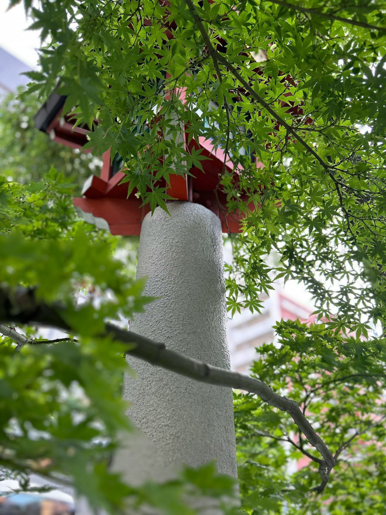 Un pilier blanc entouré de feuilles vertes avec une structure de toit rouge