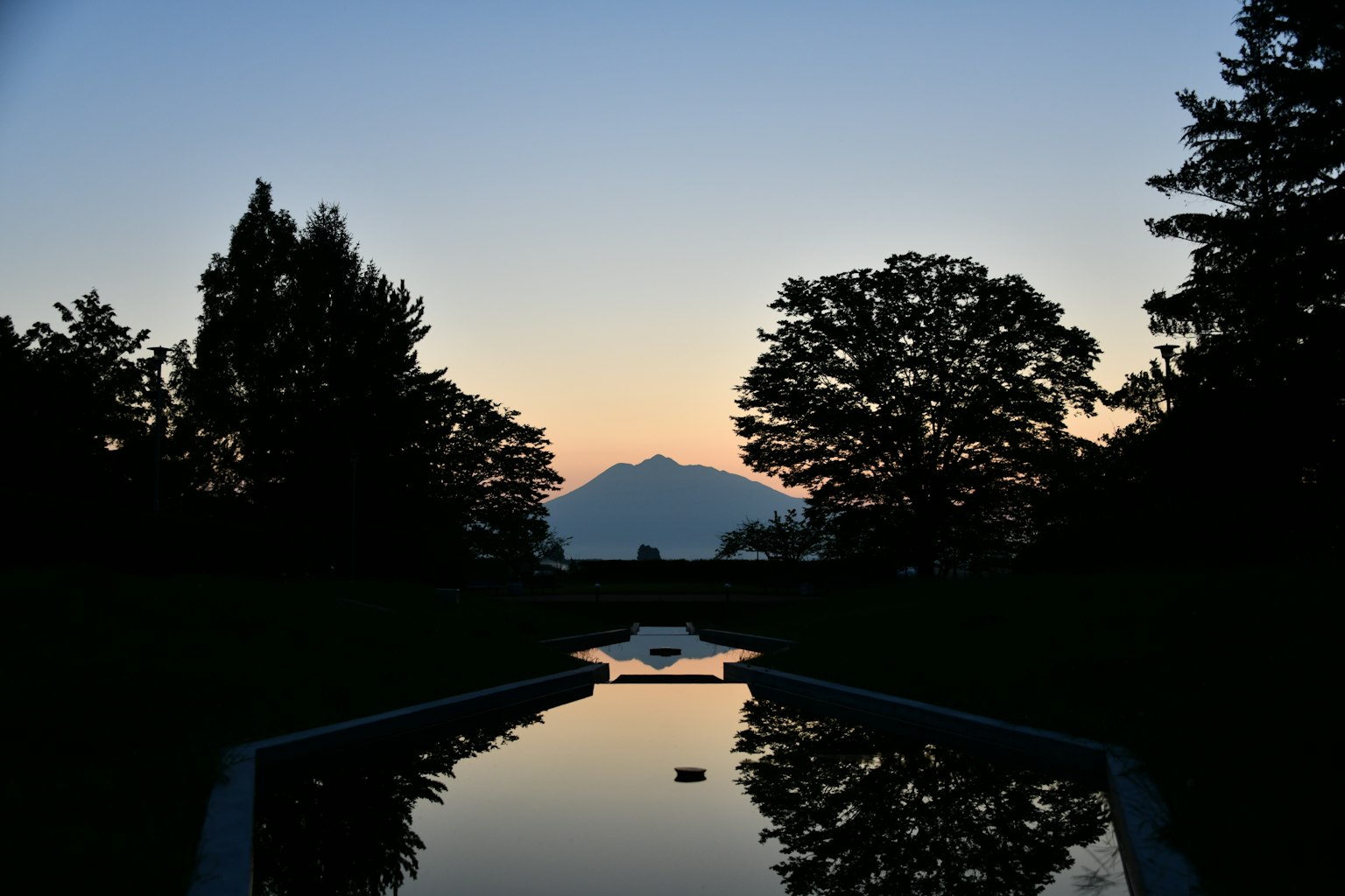 Silhouette of mountains and trees reflected in a pond at sunset