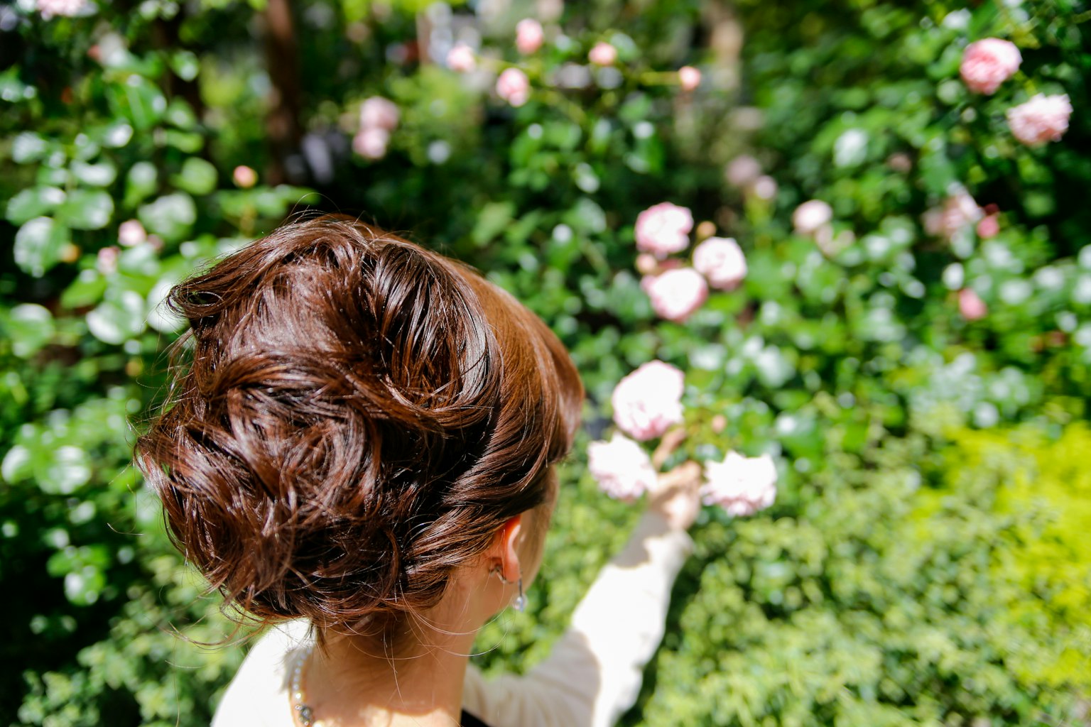 Eine Frau, die eine Blume hält und sich umdreht, mit einem üppigen grünen Hintergrund und blühenden rosa Blumen