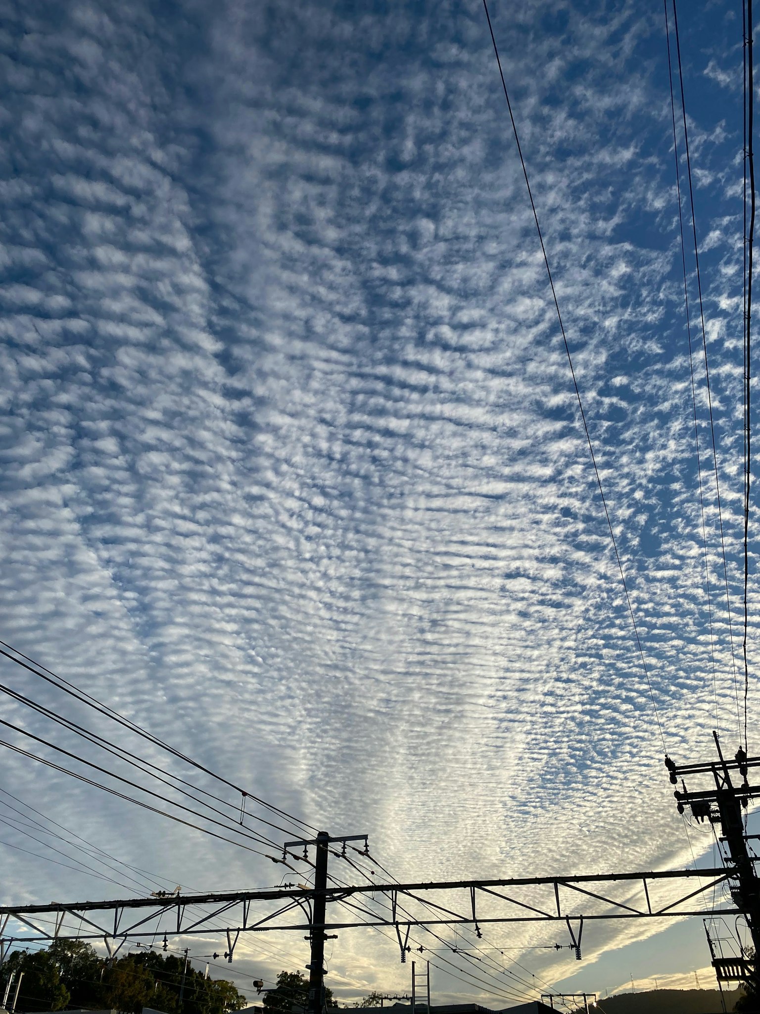 Langit biru dengan awan bergaris dan saluran listrik yang terlihat