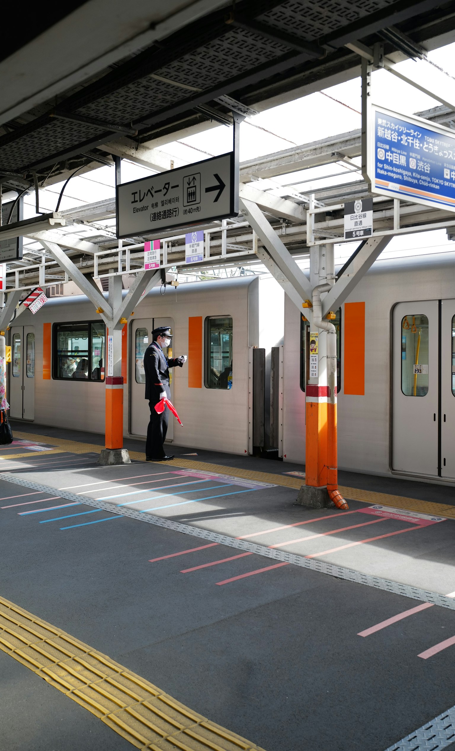 สถานีรถไฟที่มีรถไฟสีส้มและเจ้าหน้าที่ยืนอยู่