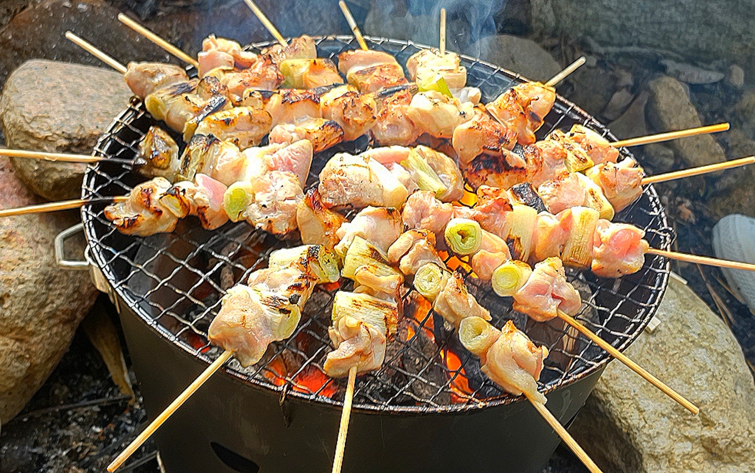 Thịt gà và rau xiên nướng trên vỉ nướng than, xung quanh có đá