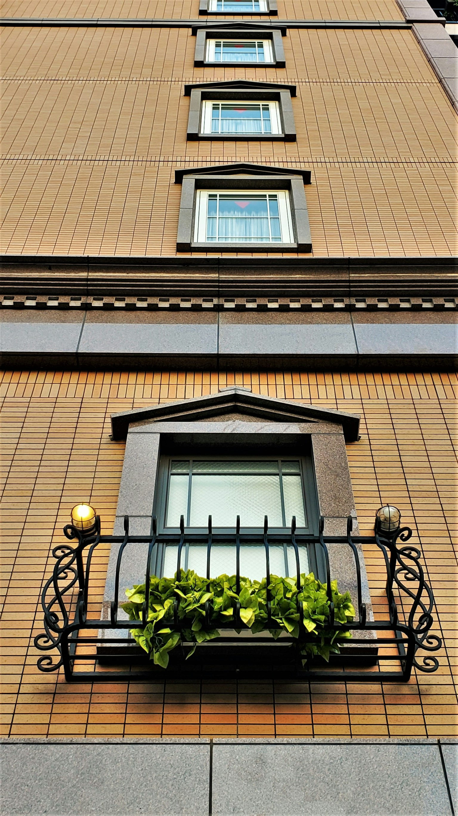 Une fenêtre avec un balcon contenant des plantes vertes sur un bâtiment en briques