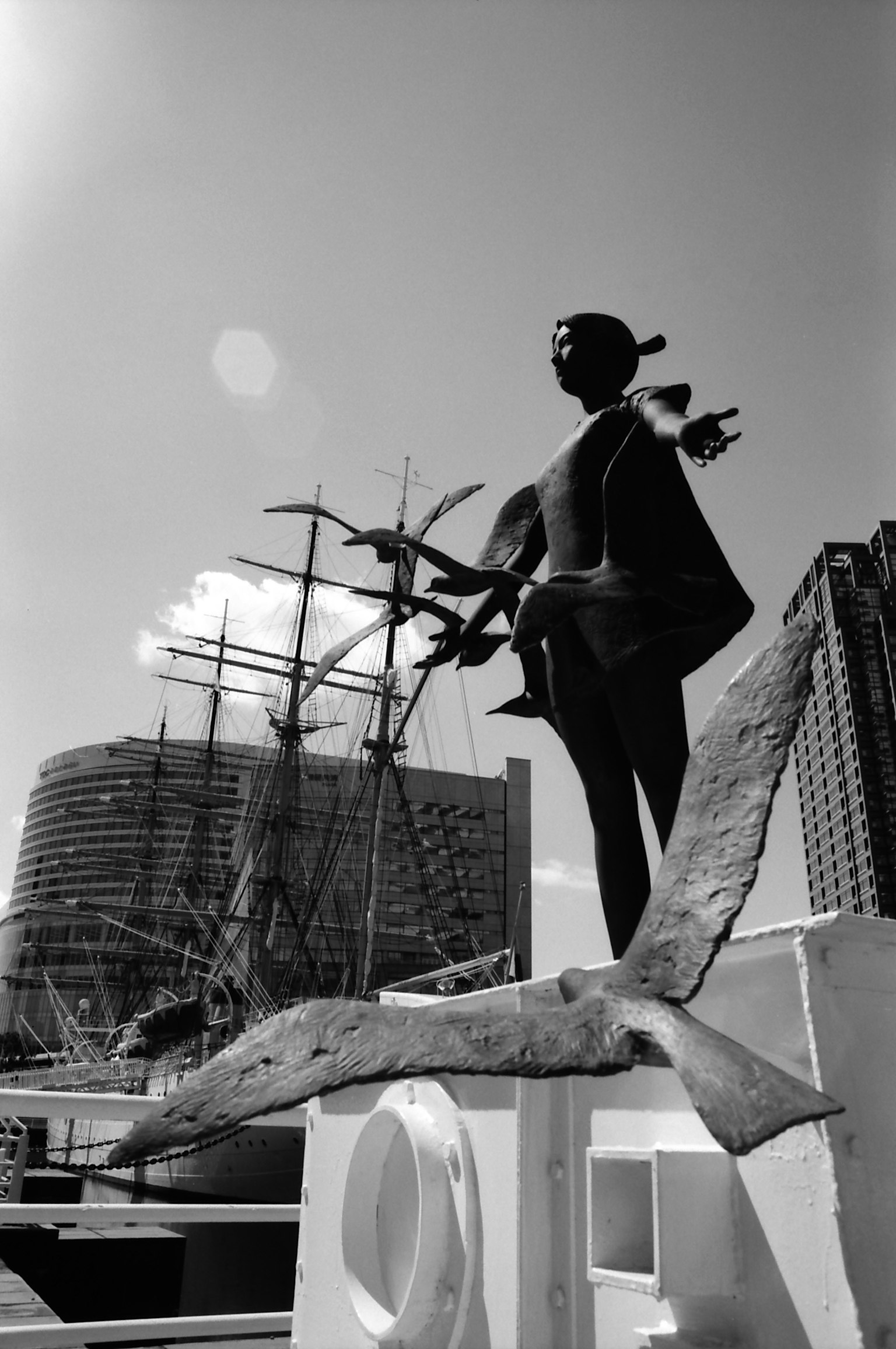 Escultura en blanco y negro de pie cerca del mar con un barco de fondo