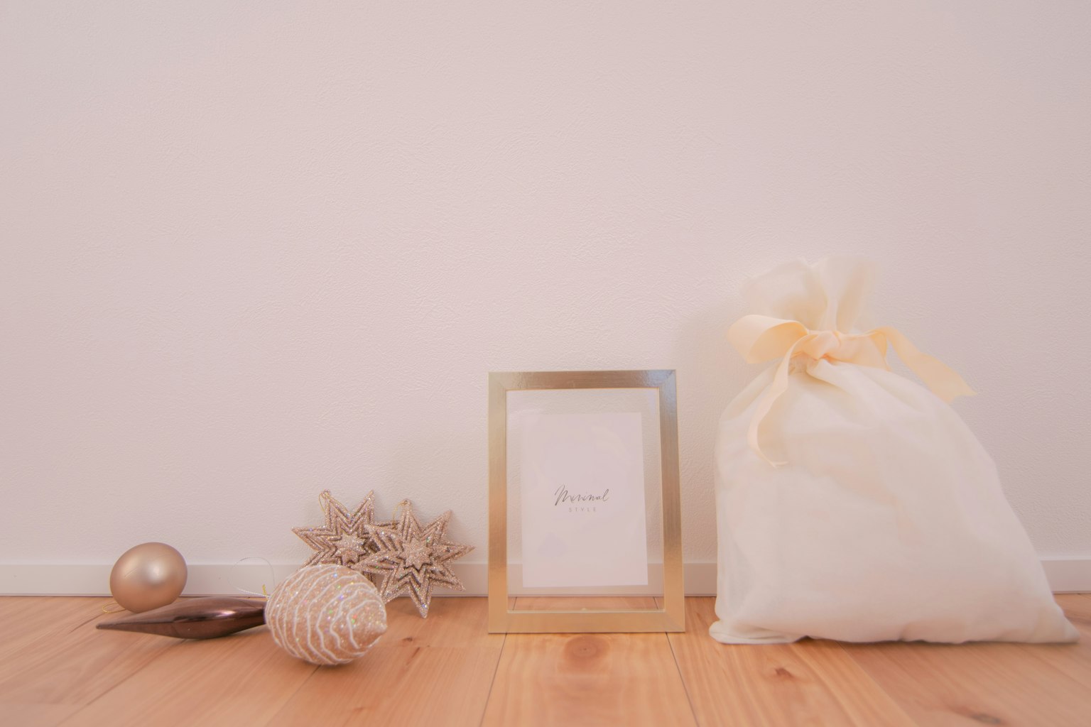 A gold-framed picture and a white ribbon-tied bag are placed in front of a white wall