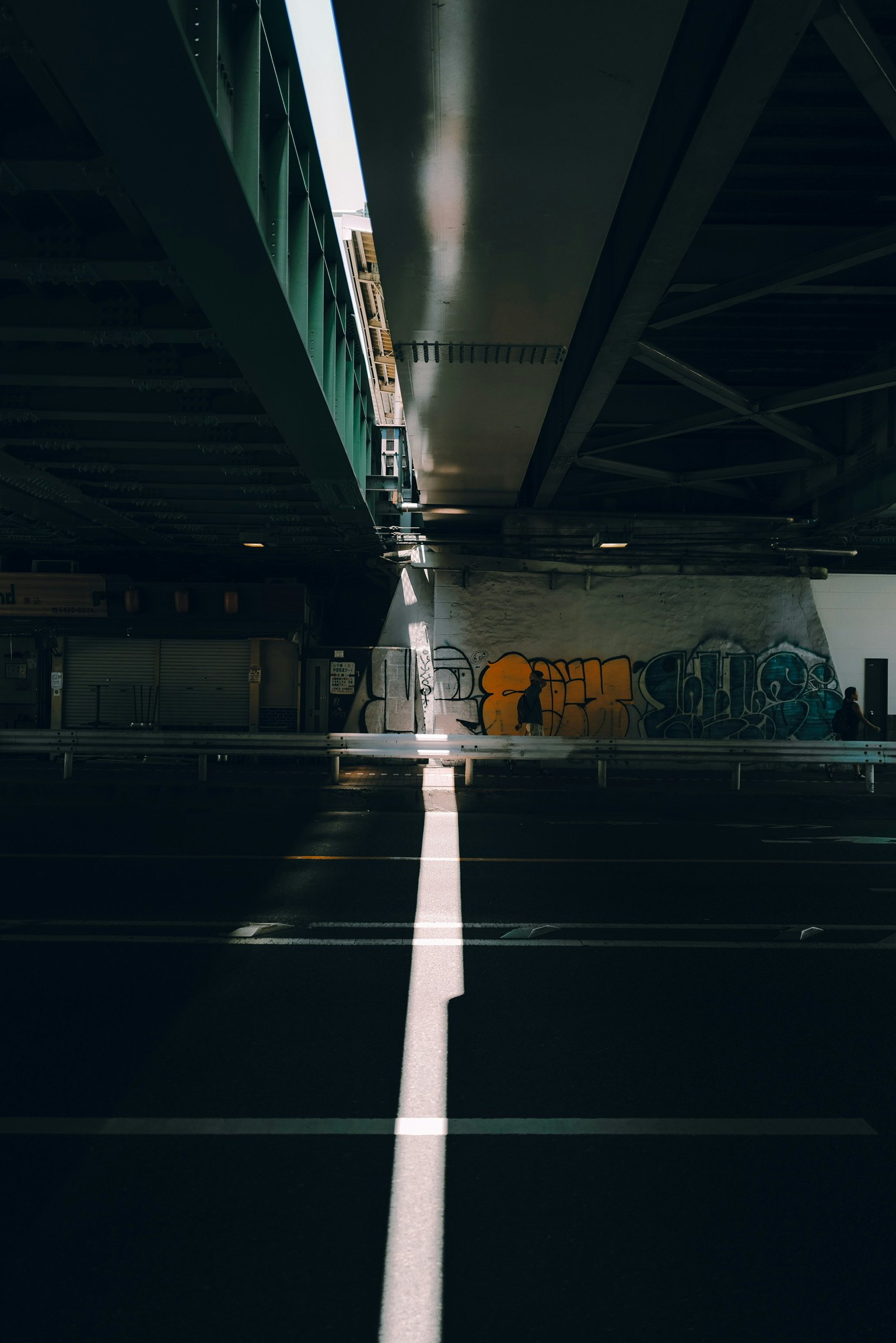 Contrasto di luce e ombra sotto un ponte con graffiti vivaci sullo sfondo