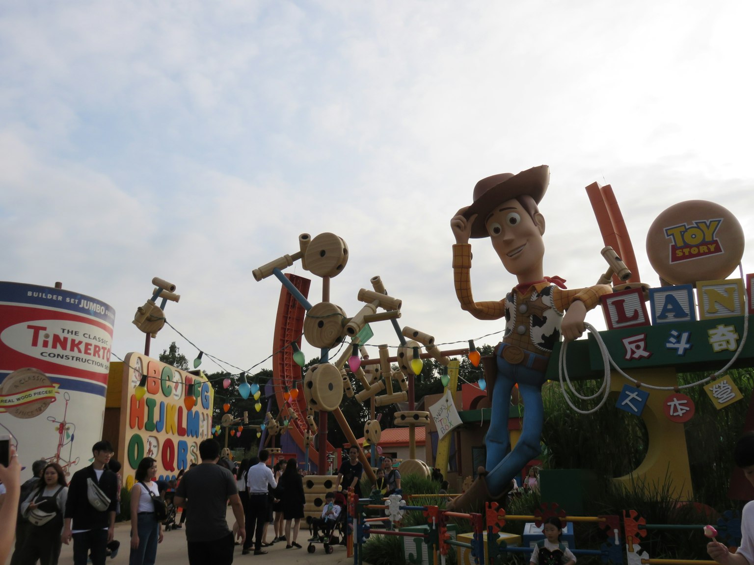 Patung Woody raksasa di taman hiburan dengan latar belakang berwarna-warni dan pengunjung