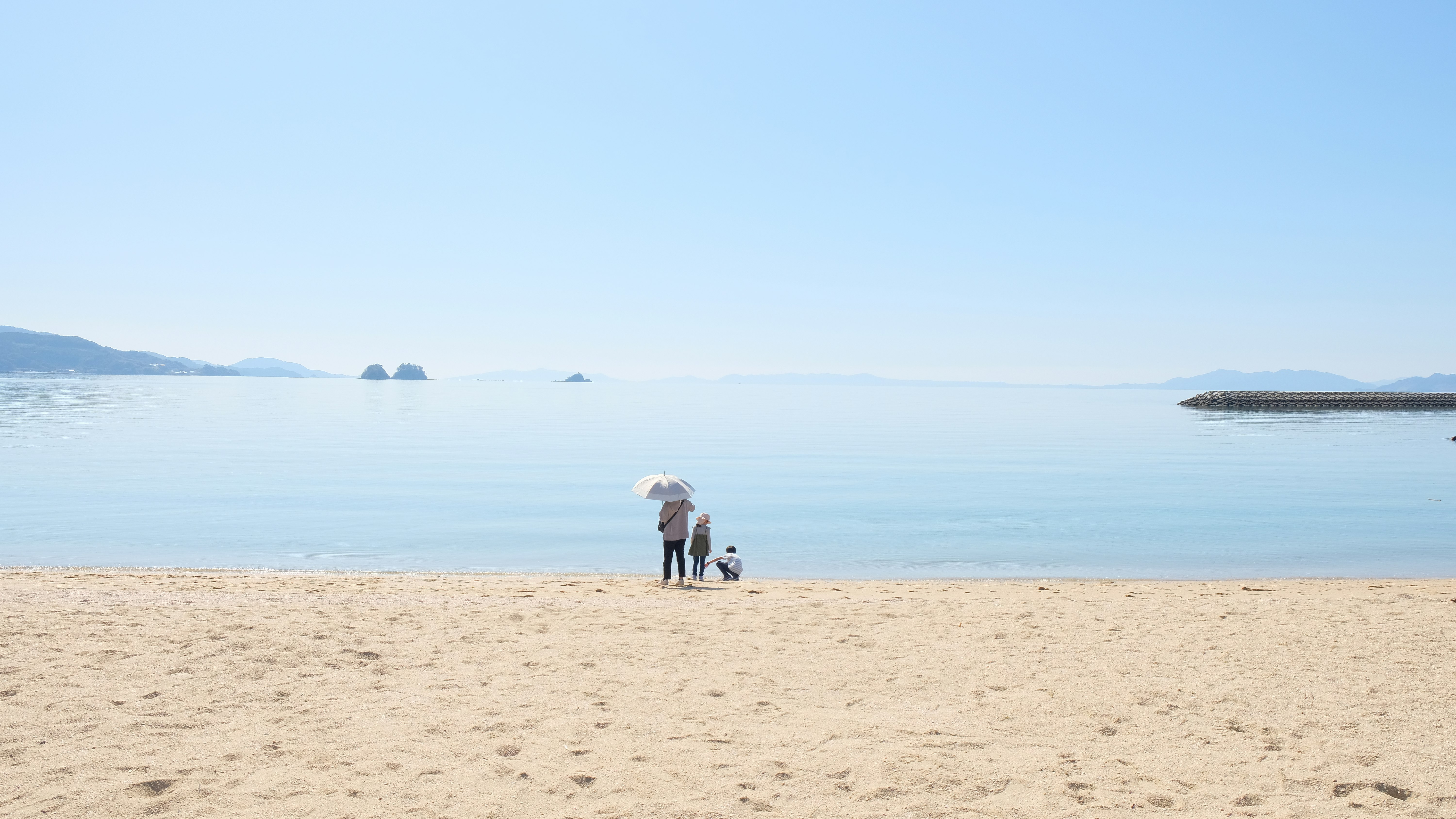 April seaside sand beach with near-empty shoreline and distant island silhouettes