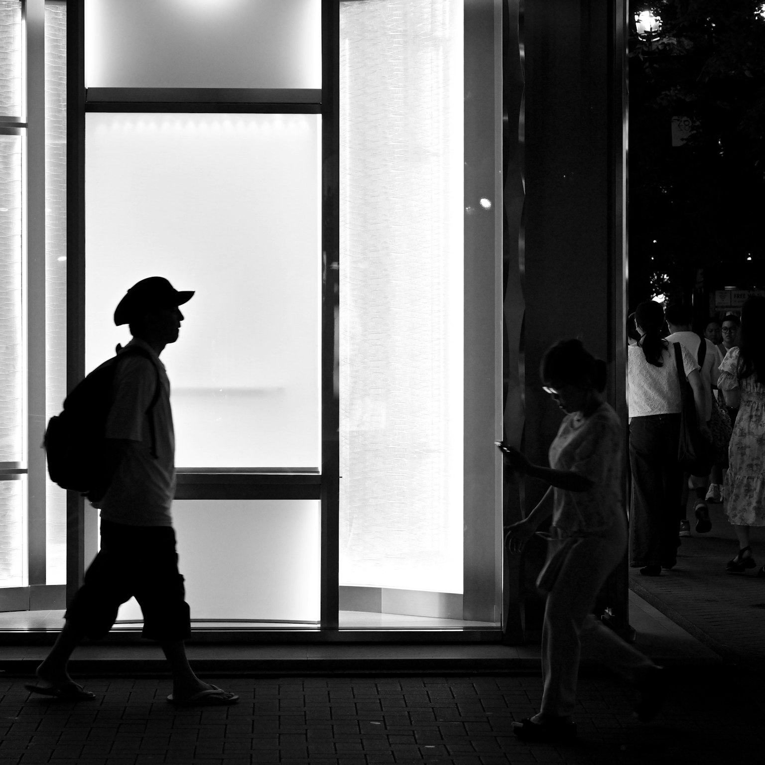 เงาของผู้คนเดินในเวลากลางคืนกับหน้าต่างร้านที่สว่าง