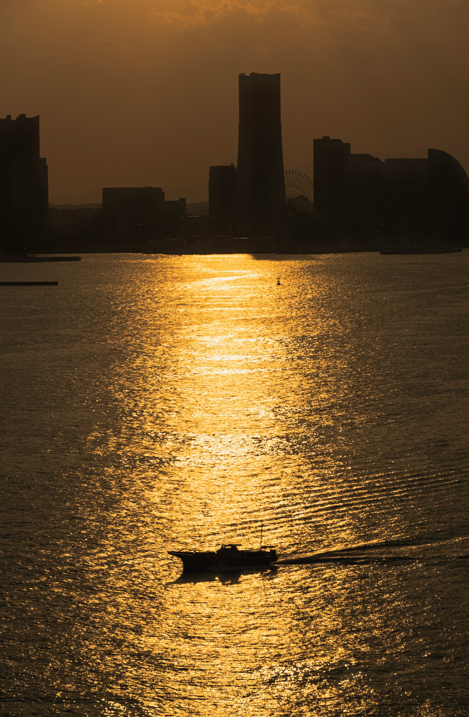 Silueta de un barco en agua brillante con el horizonte de la ciudad al atardecer