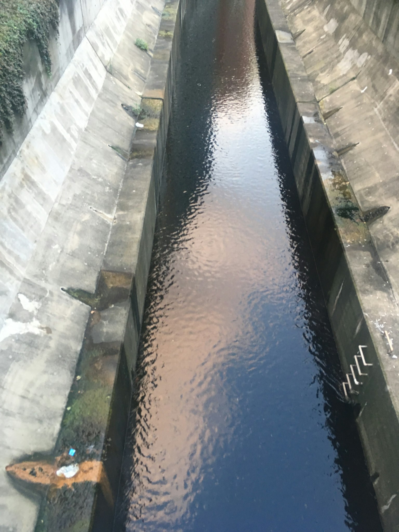 View of a dark canal with water flowing seen from above cracked concrete walls and reflections on the water surface