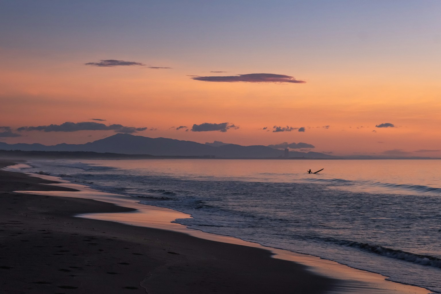 Vista di spiaggia al tramonto con onde delicate e montagne lontane
