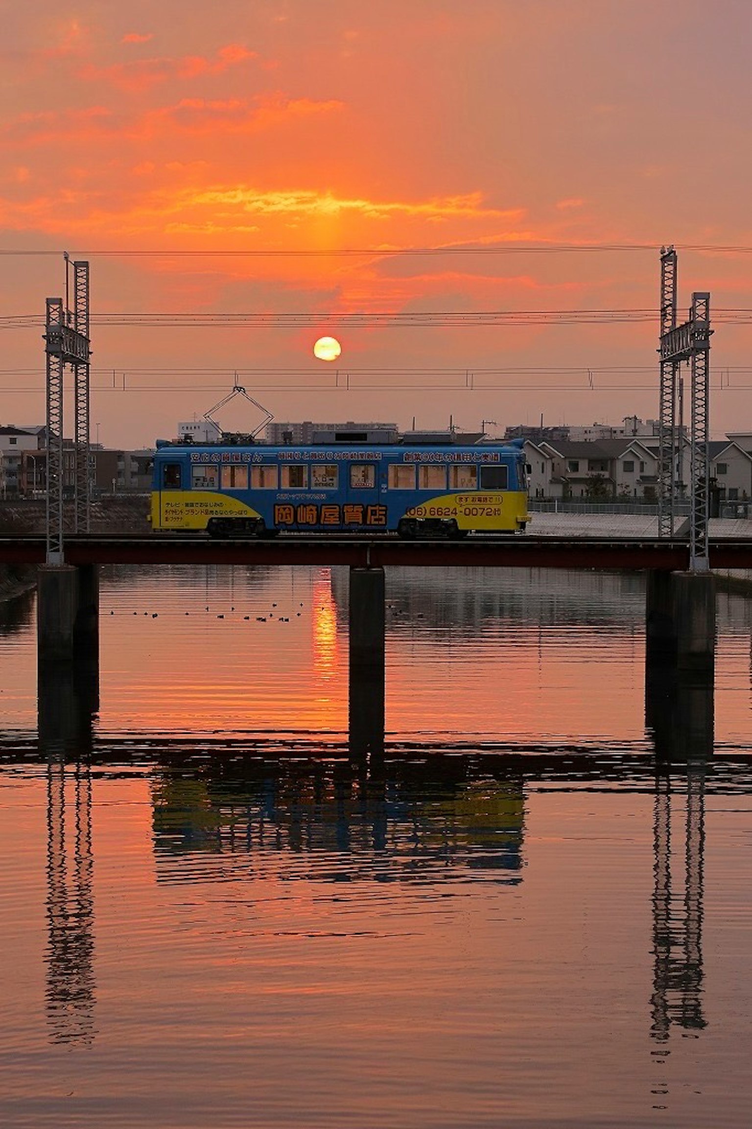Tren colorido en un puente al atardecer con reflejos en el agua