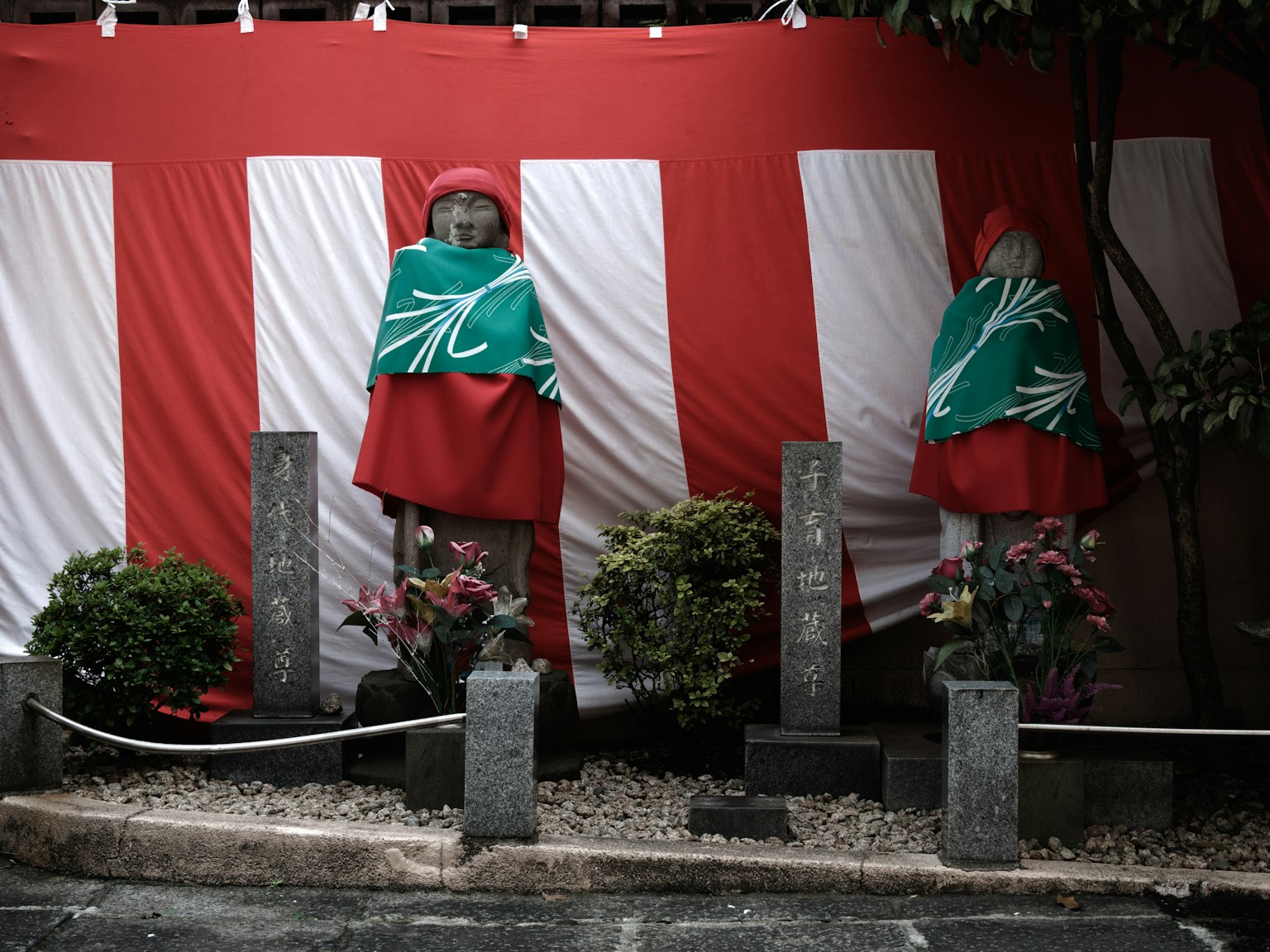 빨간 줄무늬 배경 앞에 녹색 망토를 입은 두 개의 동상과 석비가 서 있는 풍경