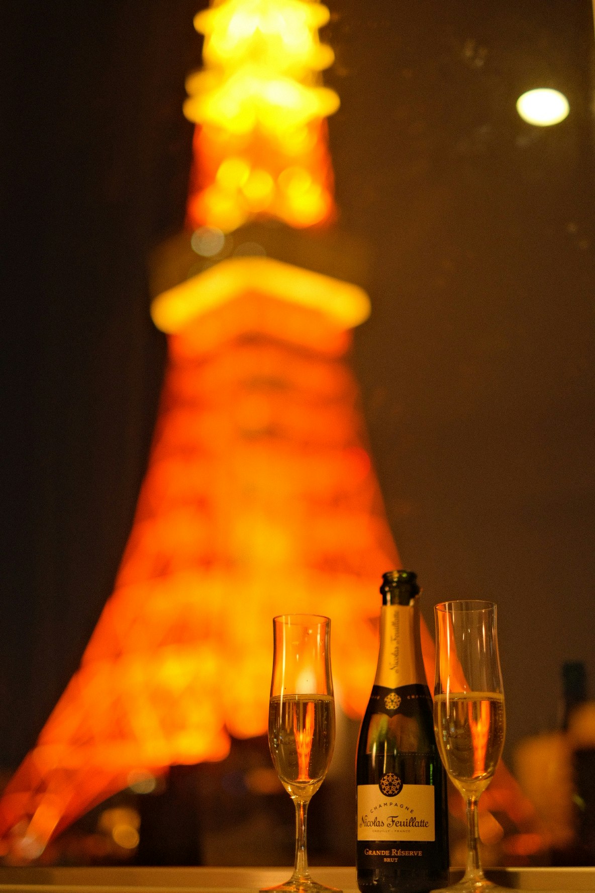botella de champán y copas con una torre iluminada al fondo