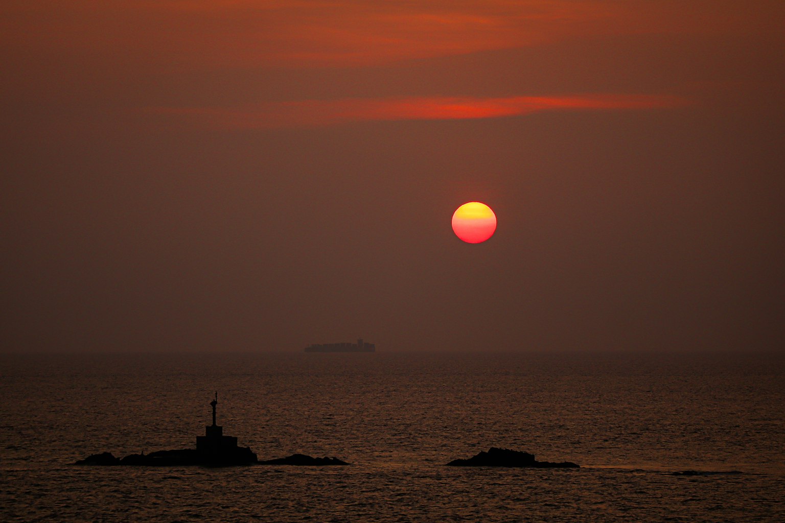 Beautiful sunset over the ocean with a small island and lighthouse visible