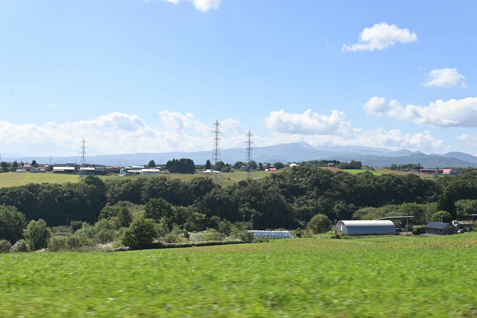 鄉村風景，綠色田野在藍天下，遠處有電線和山脈