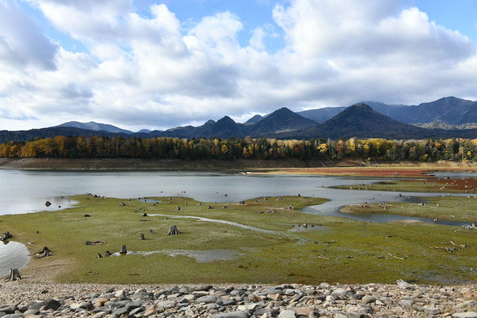 Vue pittoresque d'un lac et des montagnes avec ciel bleu et nuages Herbe et rochers éparpillés le long de la rive