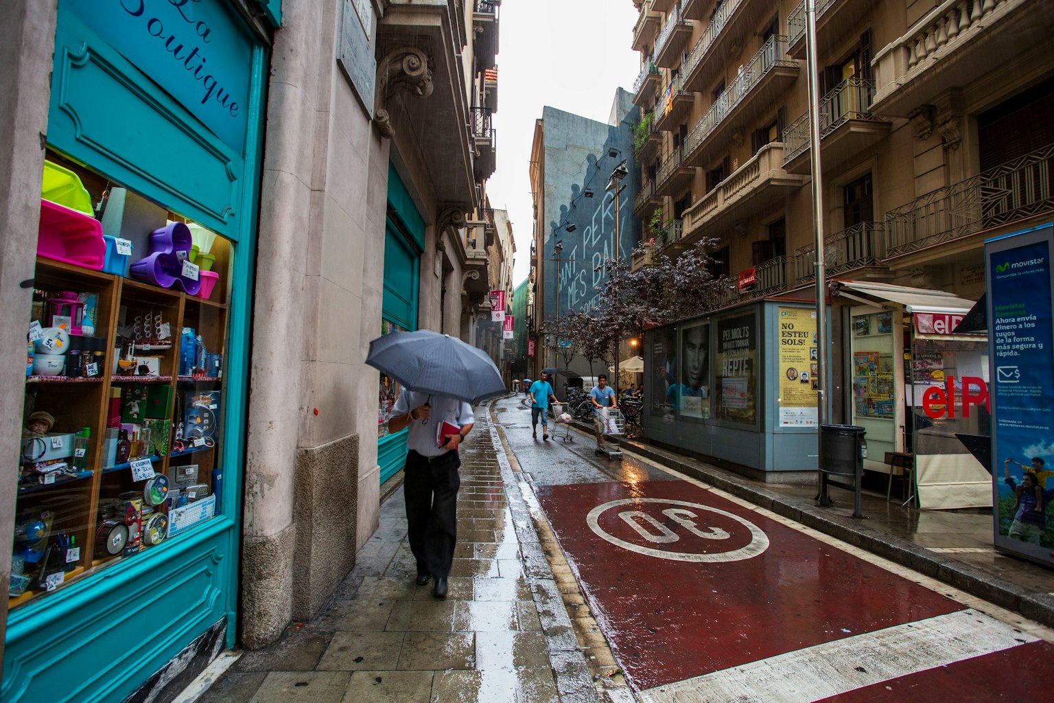 A person walking with an umbrella in the rain along a narrow street with colorful shops