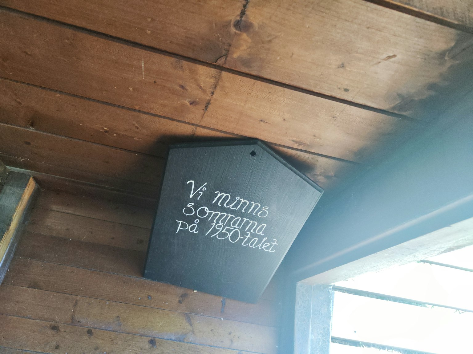 Ein schwarzes Holzschild, das an einer Holzbedeckung mit handgeschriebenem Text befestigt ist