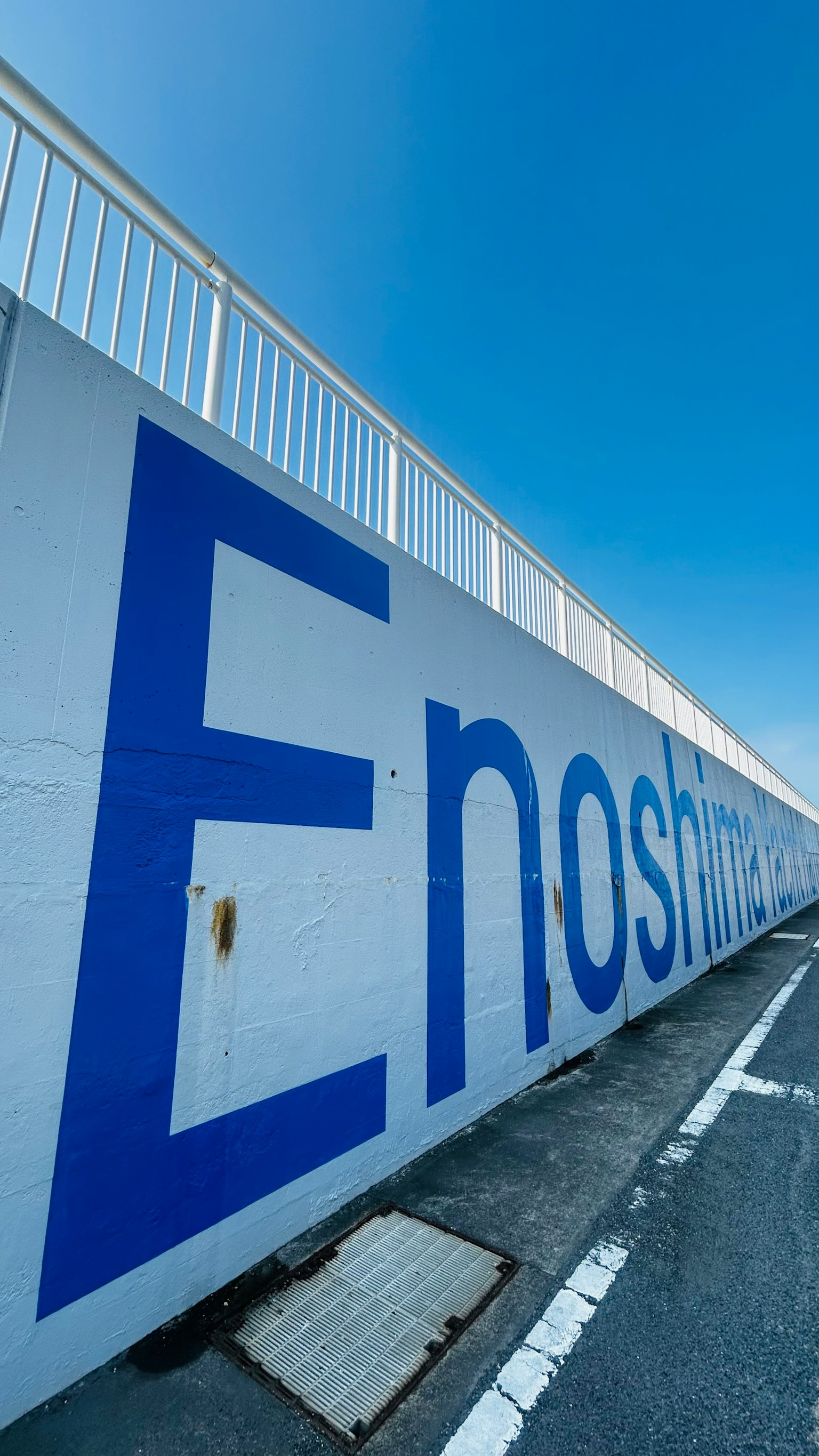 在晴朗的蓝天下，墙上用蓝色字母写着'Enoshima'的巨大白色墙壁