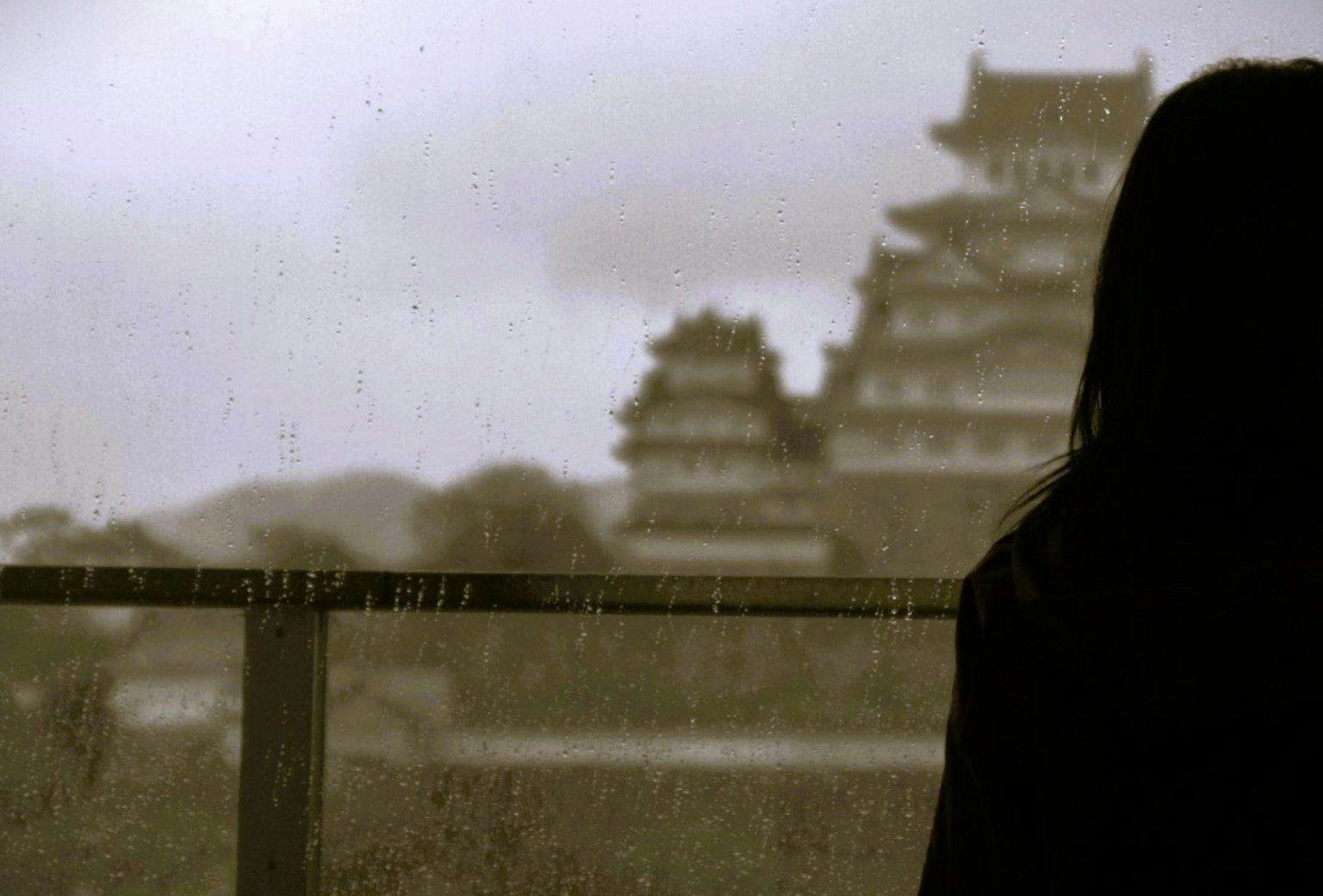Silhouette di una donna con il castello di Himeji sotto la pioggia