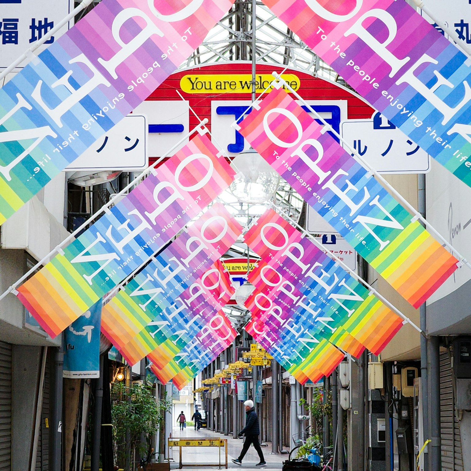 Una strada commerciale colorata con striscioni appesi e una persona che cammina