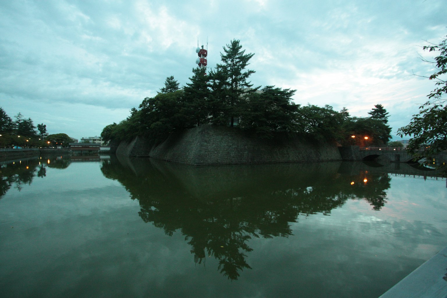 A tranquil lake reflecting a lush green island and overcast sky