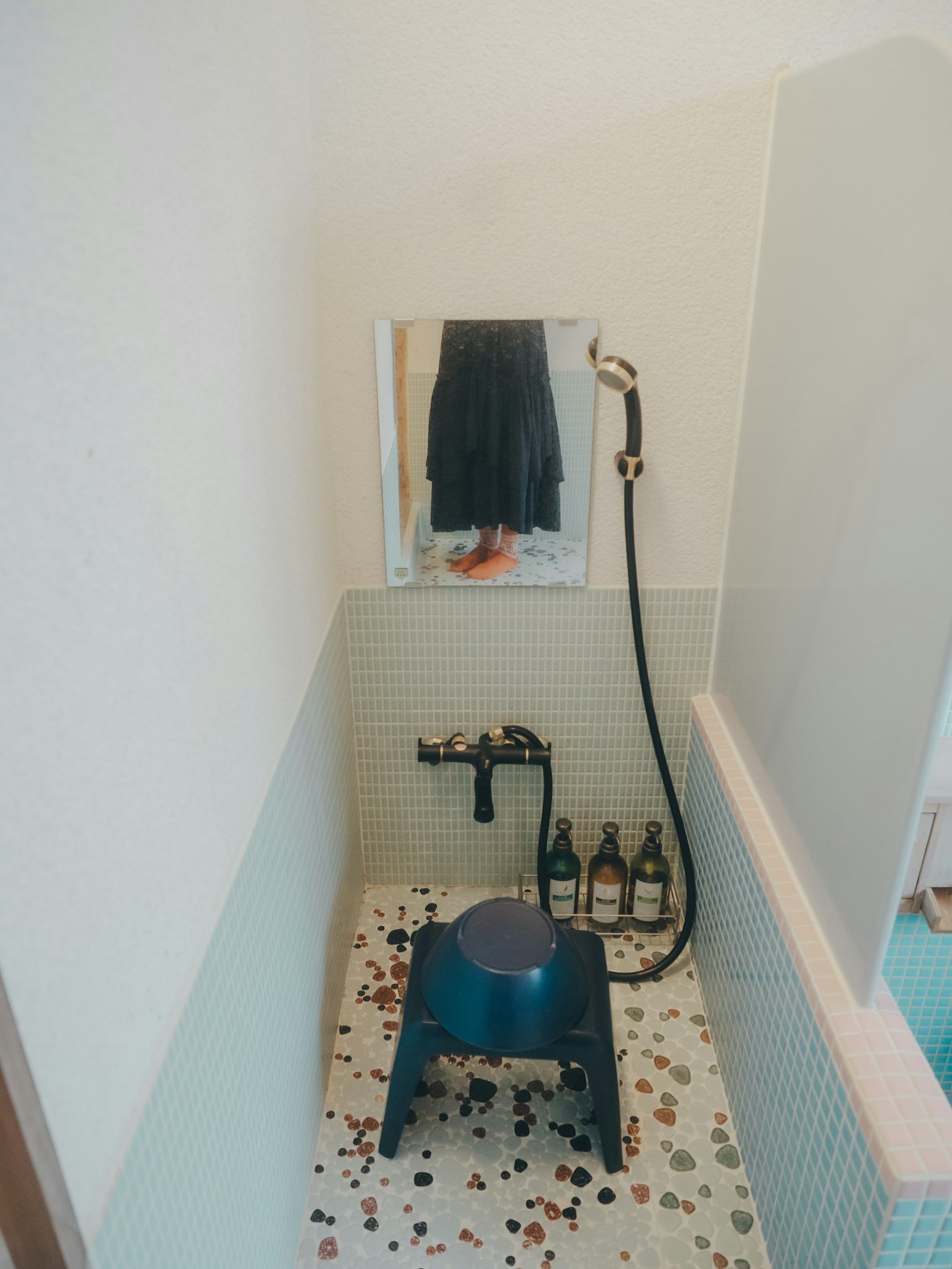 Eine Ecke eines einfachen Badezimmers mit einem blauen Hocker und einer Dusche