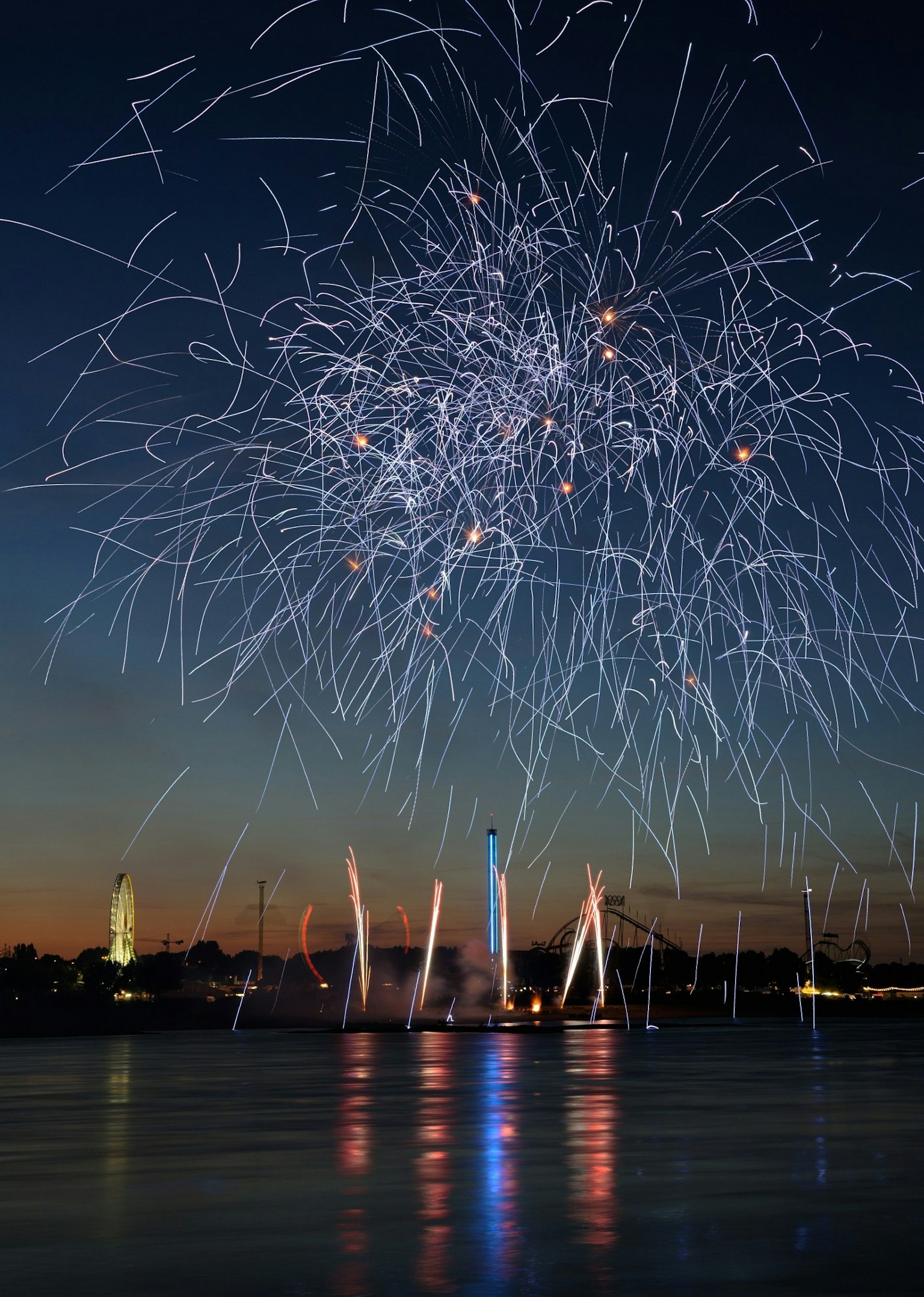 Feuerwerk, das im Nachthimmel explodiert, mit Reflexionen auf dem Wasser
