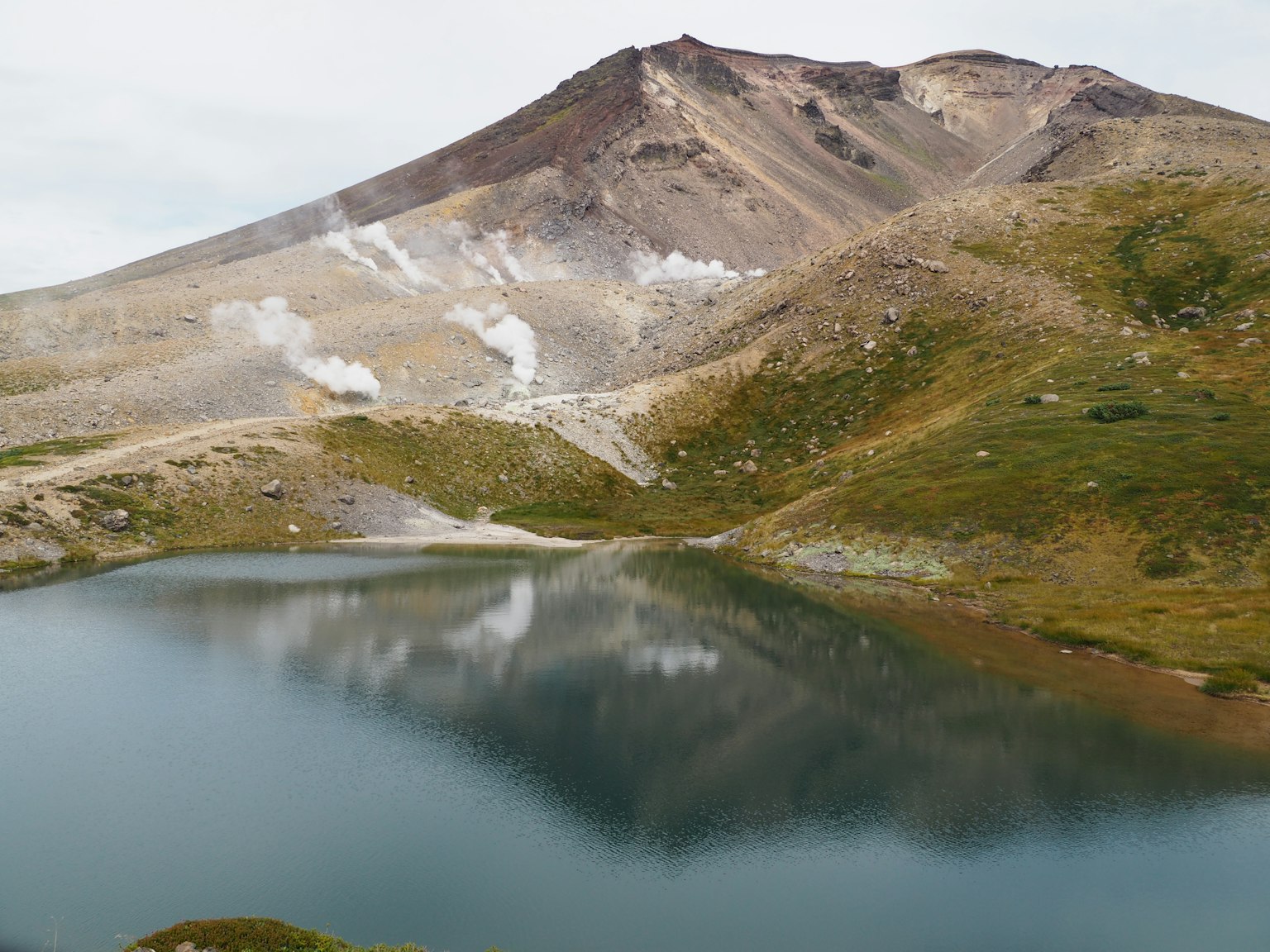 Danau indah yang mencerminkan gunung dengan uap yang naik dari lereng