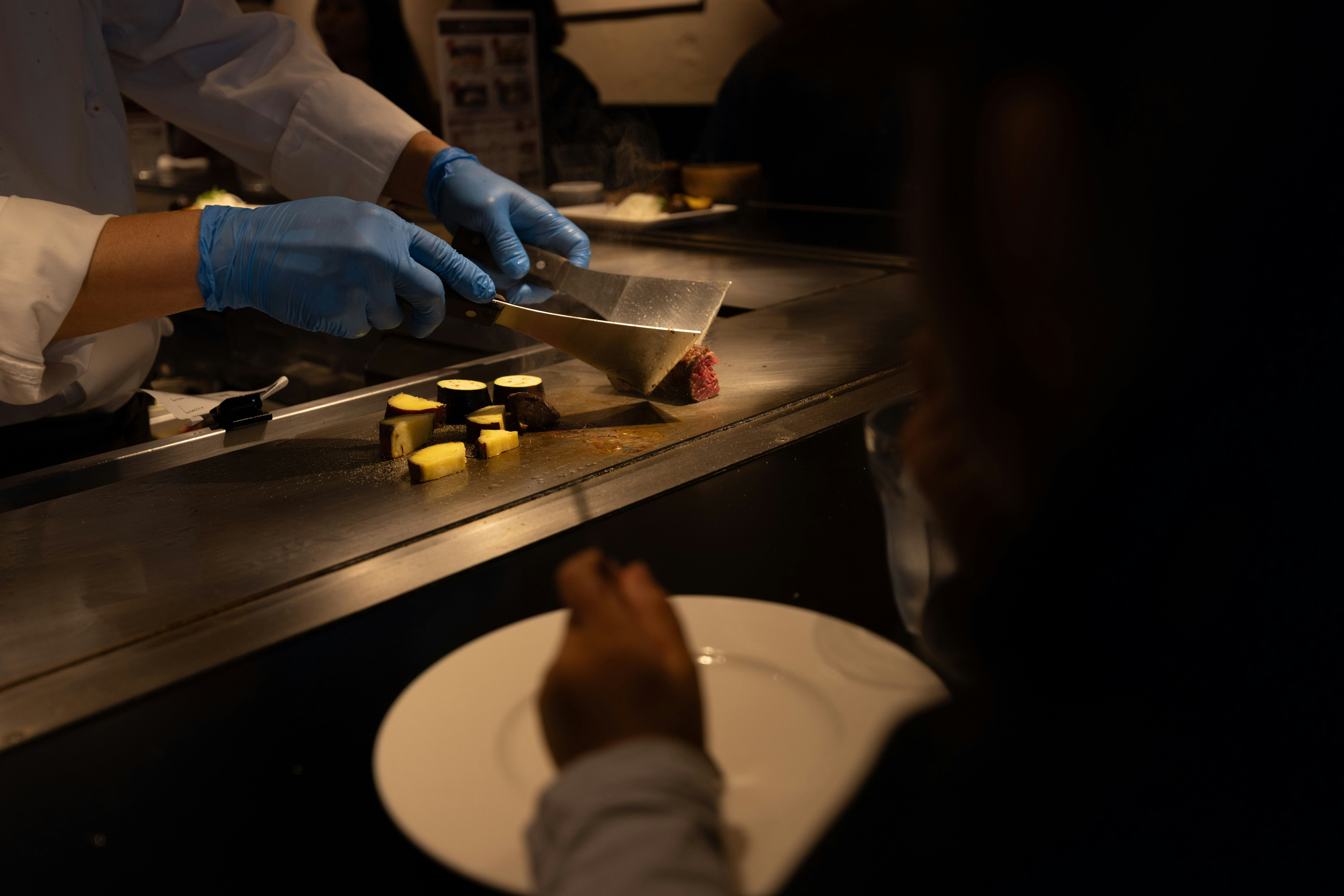 cuisinier ganté finissant un plat au couteau dans une cuisine