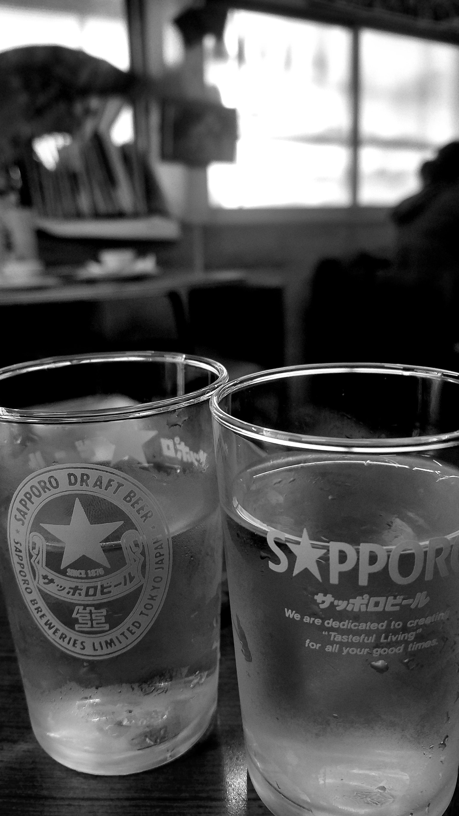 Due bicchieri con logo Sapporo e acqua su un tavolo di legno in un ambiente in bianco e nero