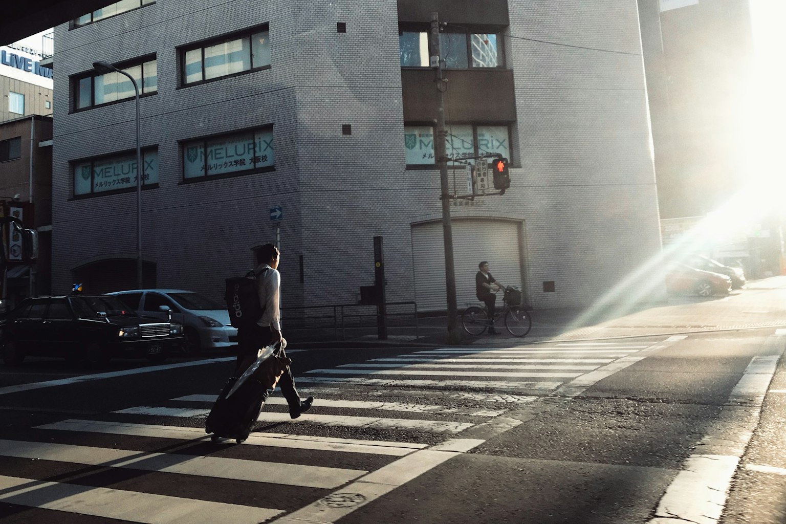 Un uomo che attraversa la strada con una valigia alla luce del sole