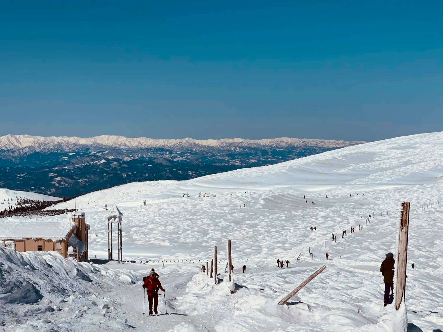 Snow-covered mountain landscape with hikers walking under a clear blue sky