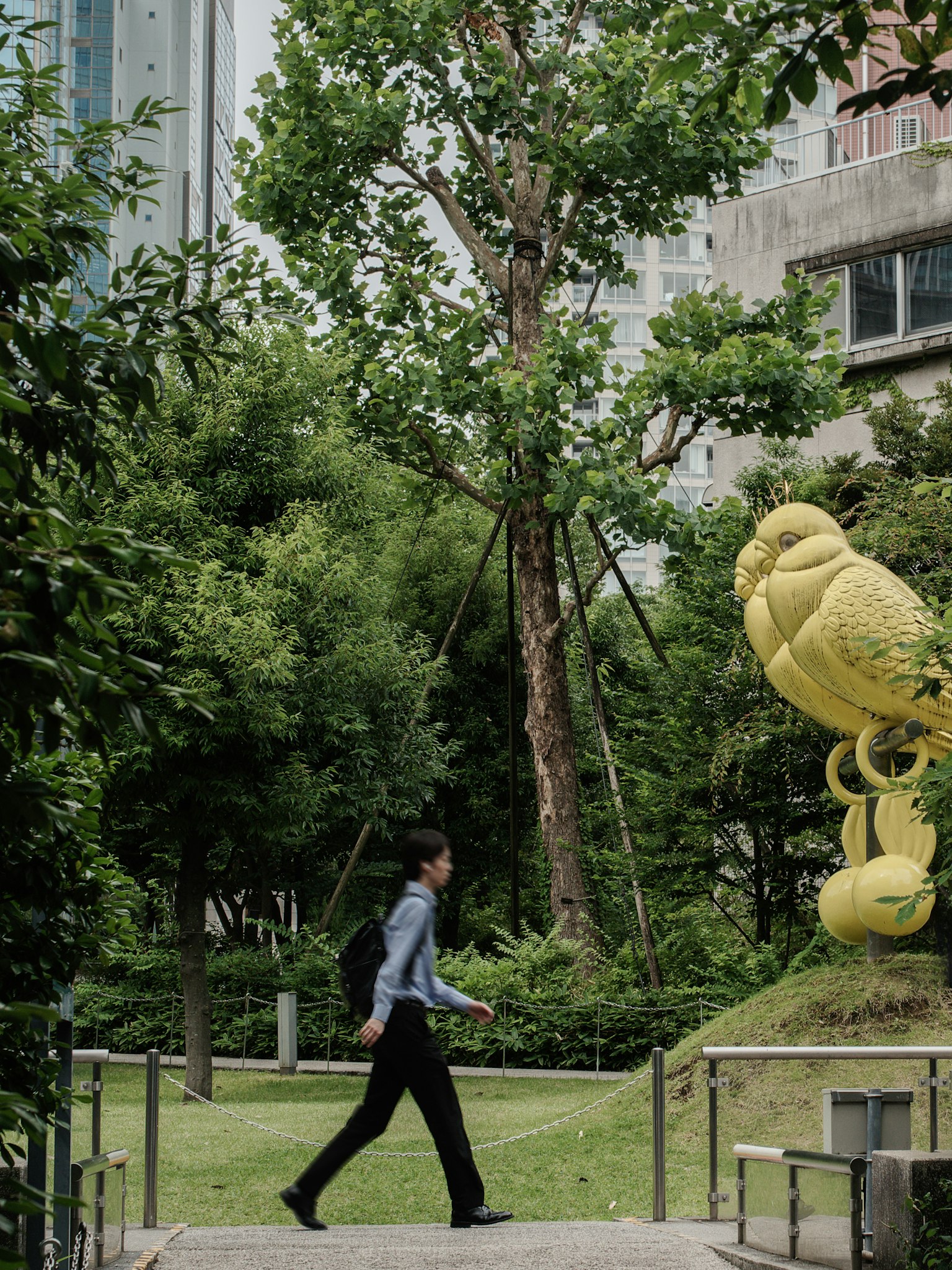 Uomo d'affari che cammina in un parco verde con una scultura gialla