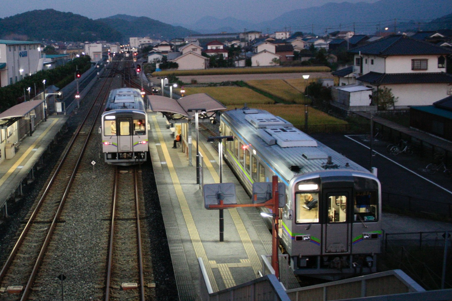 Kereta di stasiun saat senja dengan area pemukiman di dekatnya