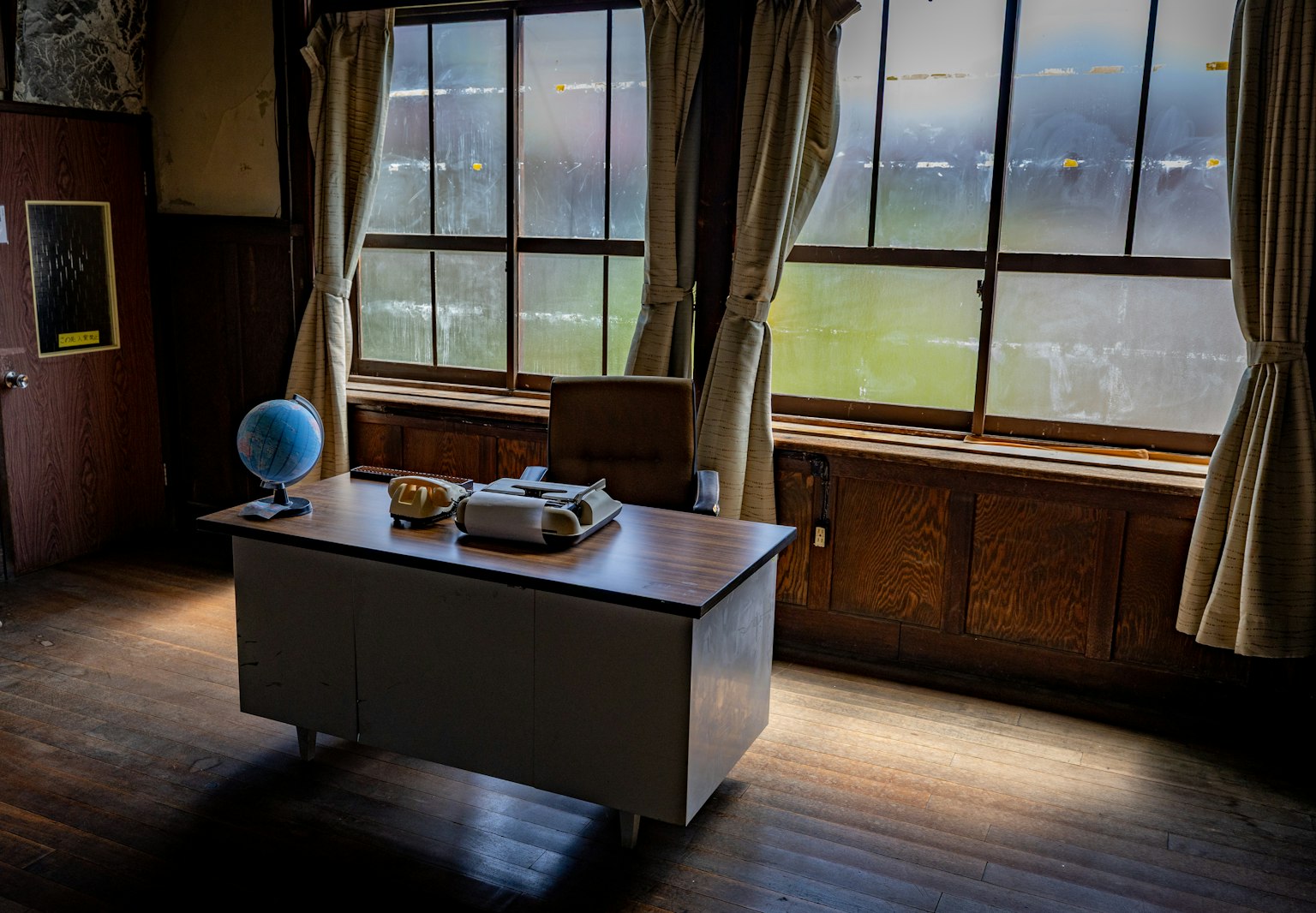 Interior de una oficina con ventanas grandes un escritorio y una silla un globo y pequeños objetos sobre el escritorio