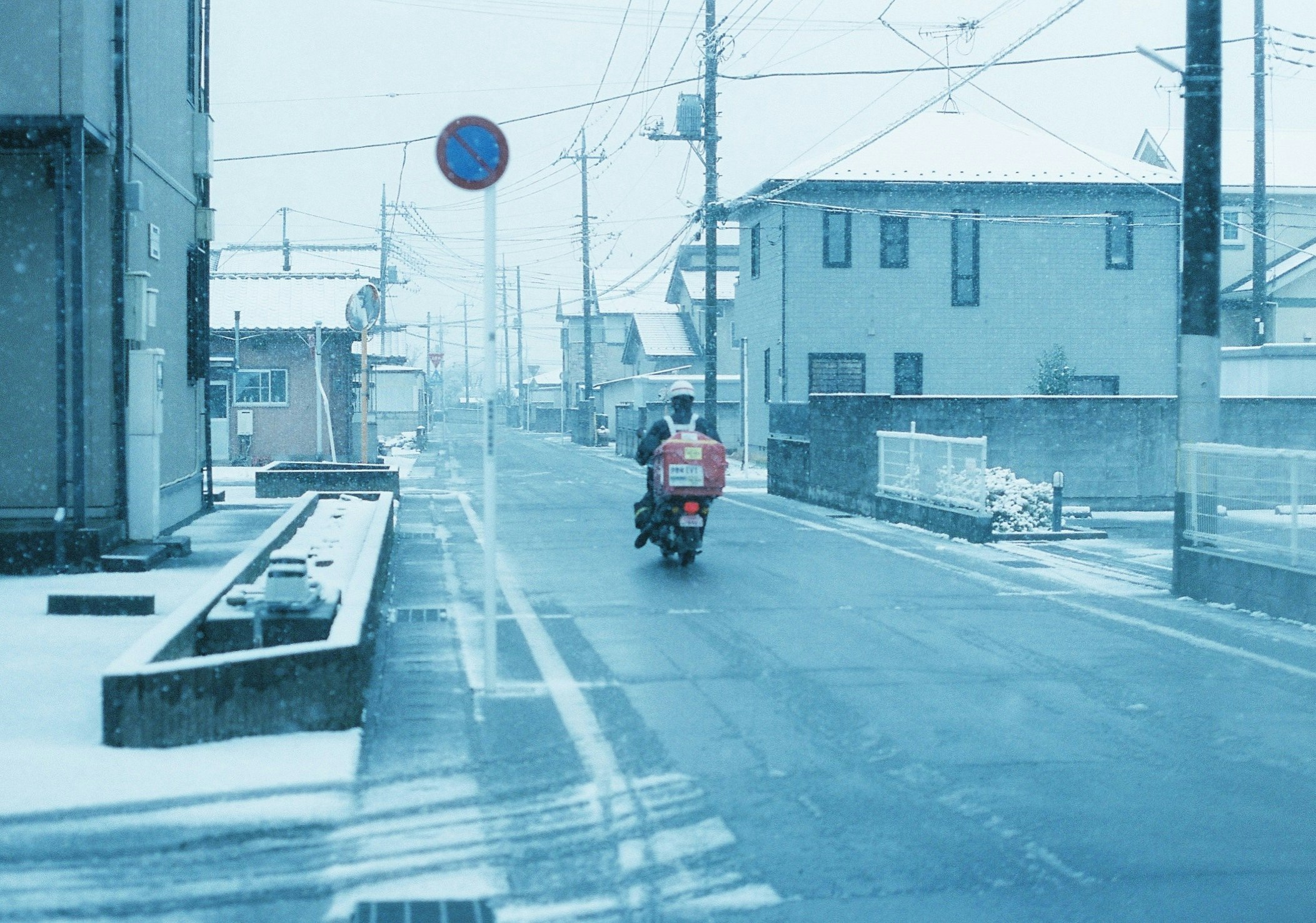 雪の路地を走るバイクのある街並み
