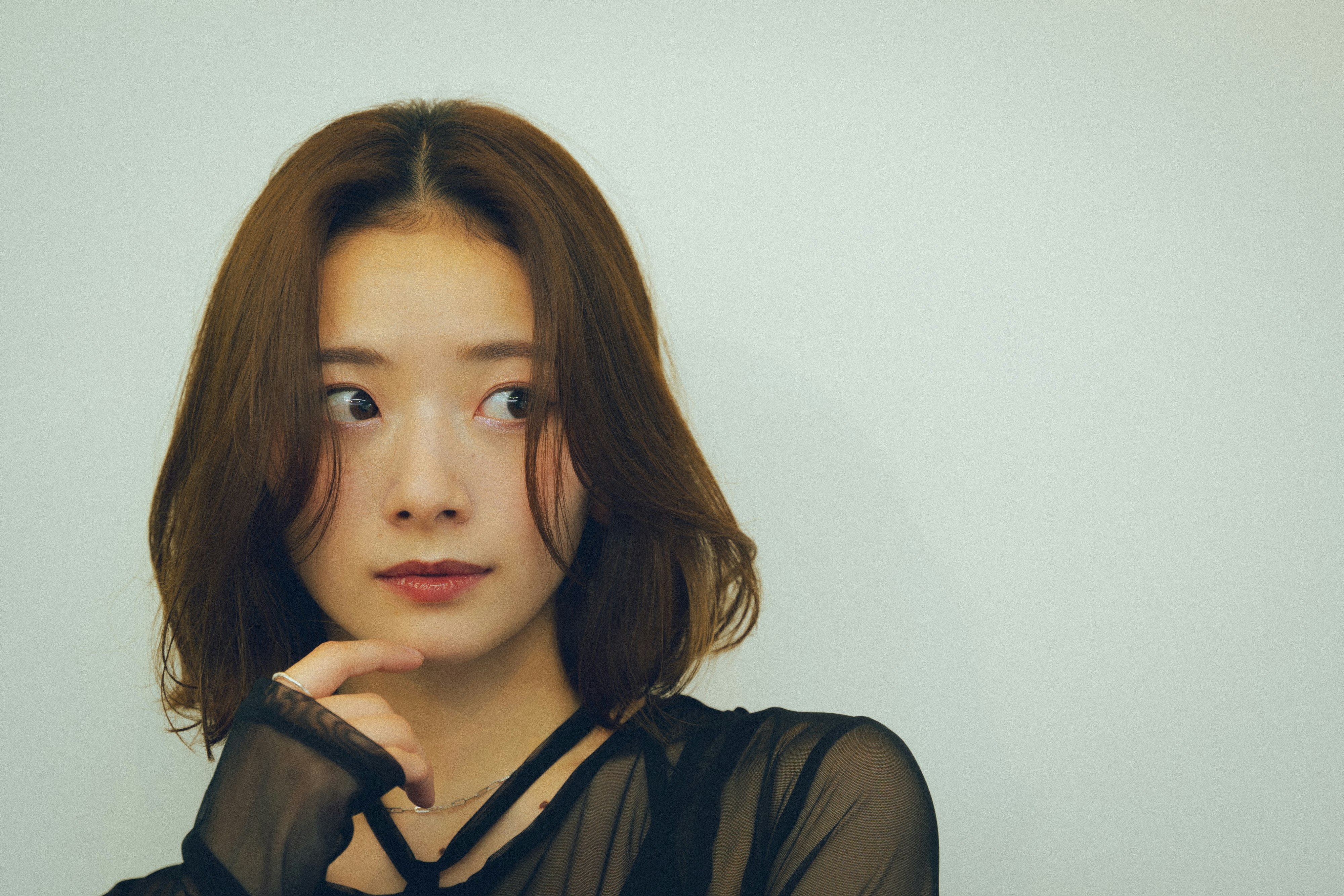 黒い服の女性が手を添えて見つめるポートレート