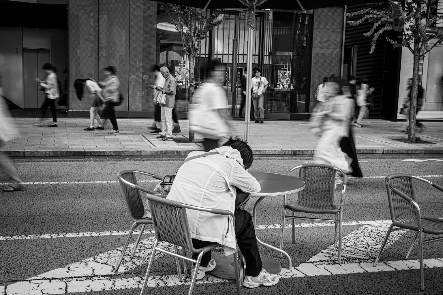 街の中で椅子に座り、頭を抱える人々の流れの中で静かに佇む人物