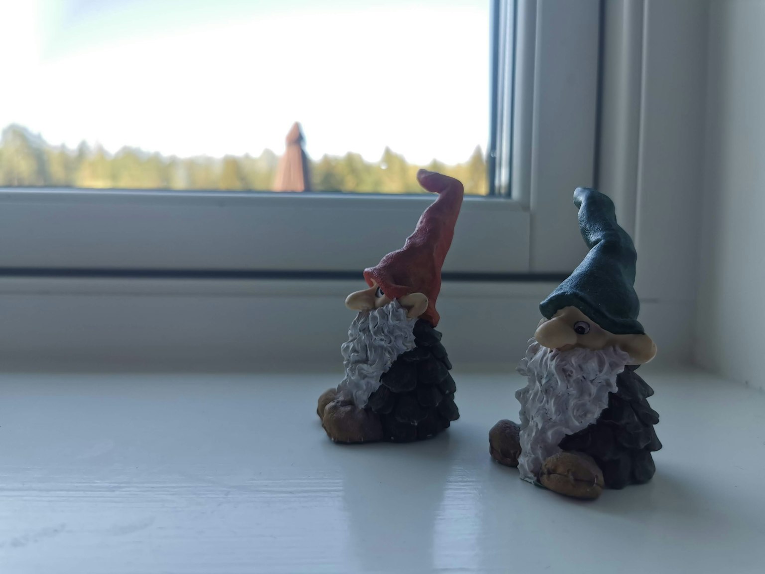 Dua patung kecil gnome taman duduk di dekat jendela mengenakan topi merah dan biru