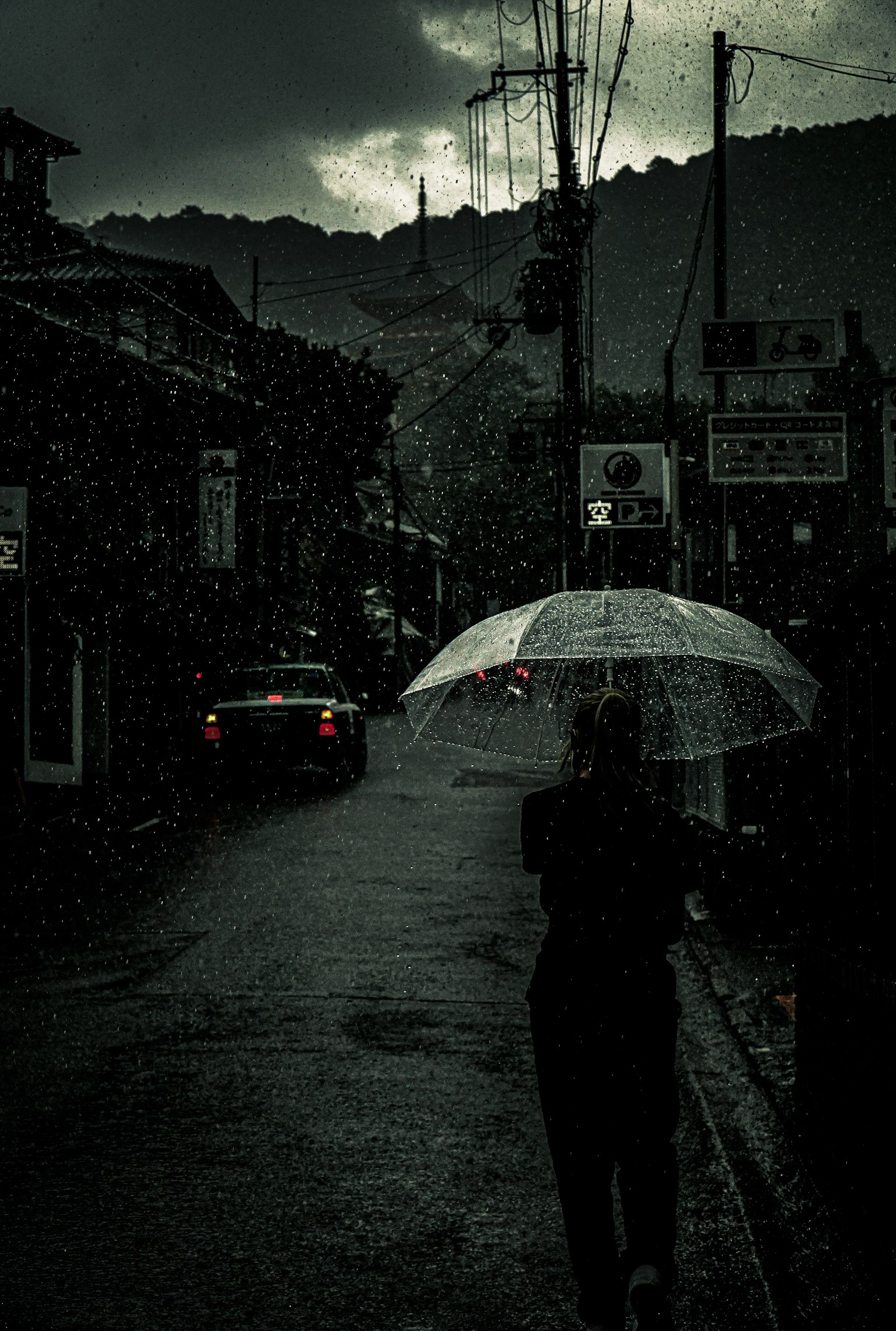 雨の中で傘をさして歩く人物と暗い街並み