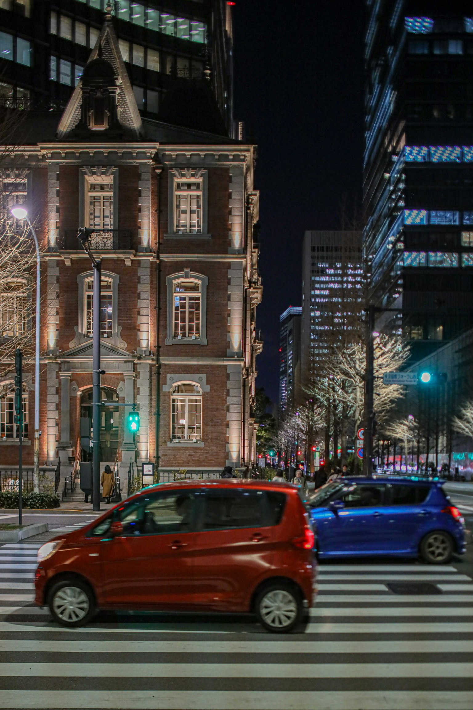 Auto rosse e blu che attraversano l'incrocio di notte con un edificio storico sullo sfondo