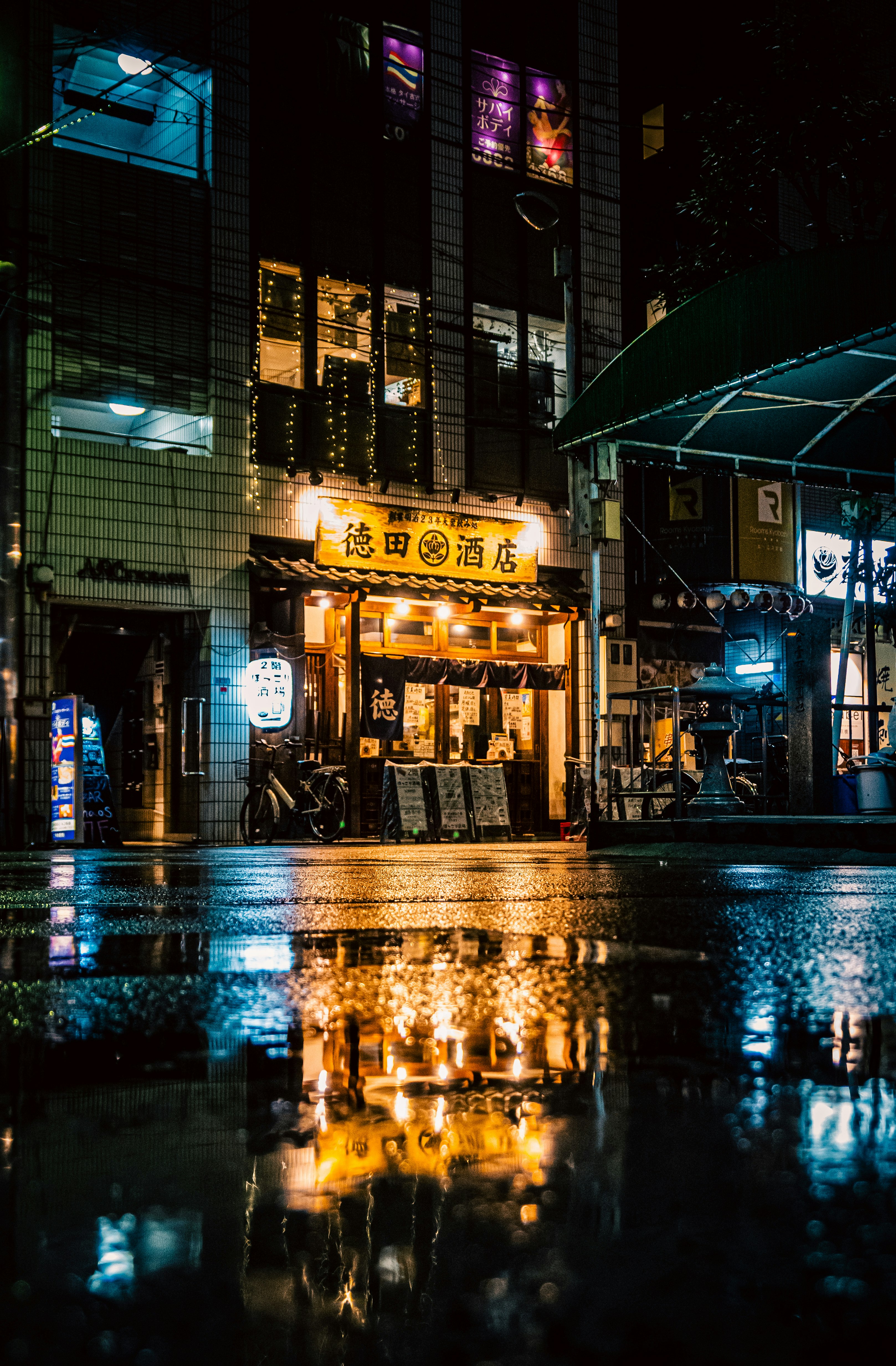 雨の夜に光る看板が並ぶ街角の居酒屋前