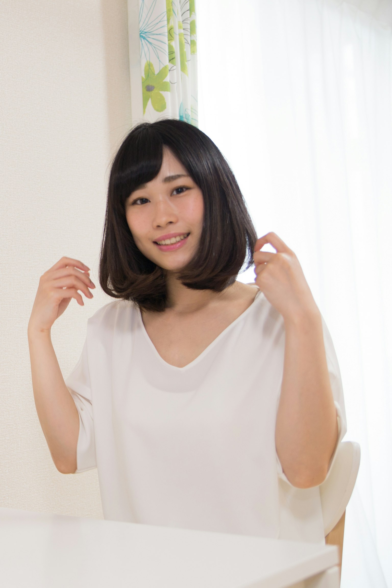 A woman in a white shirt smiling while adjusting her hair