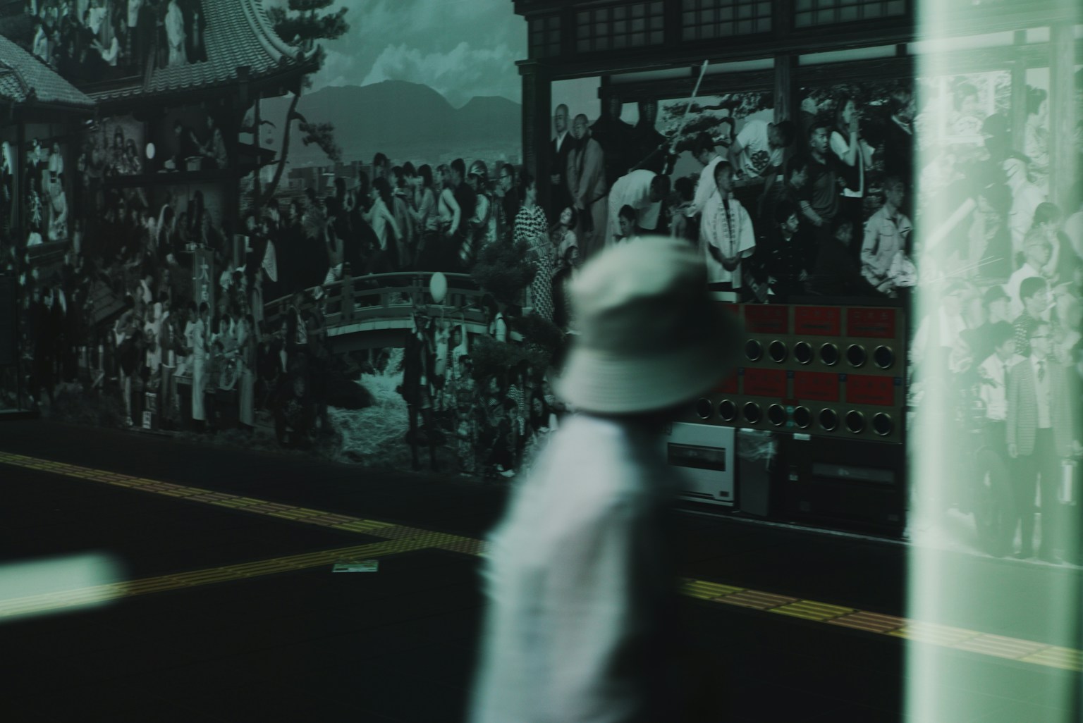 Blurred figure wearing a hat walking in front of a crowd-filled background