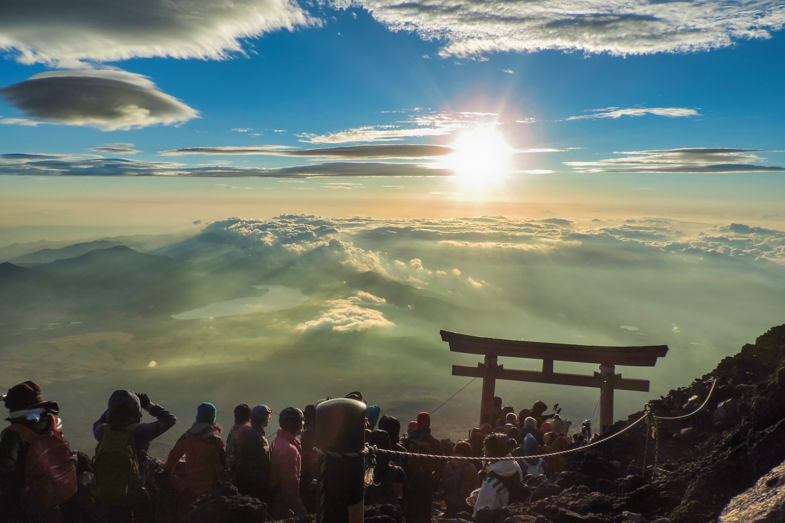 후지산 정상에서 구름 위로 떠오르는 멋진 일출과 토리이 게이트와 관광객들