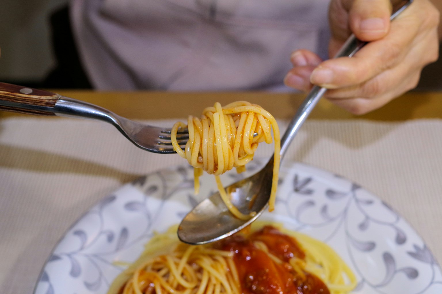 Sebuah tangan yang memutar spageti dengan garpu dan sendok