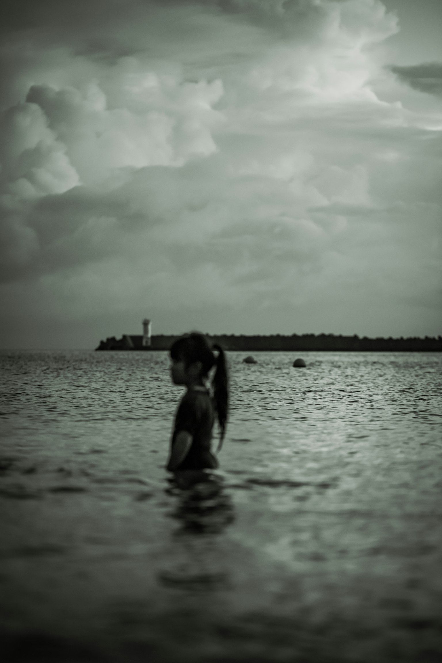 Siluet seorang gadis berdiri di laut dengan mercusuar di latar belakang